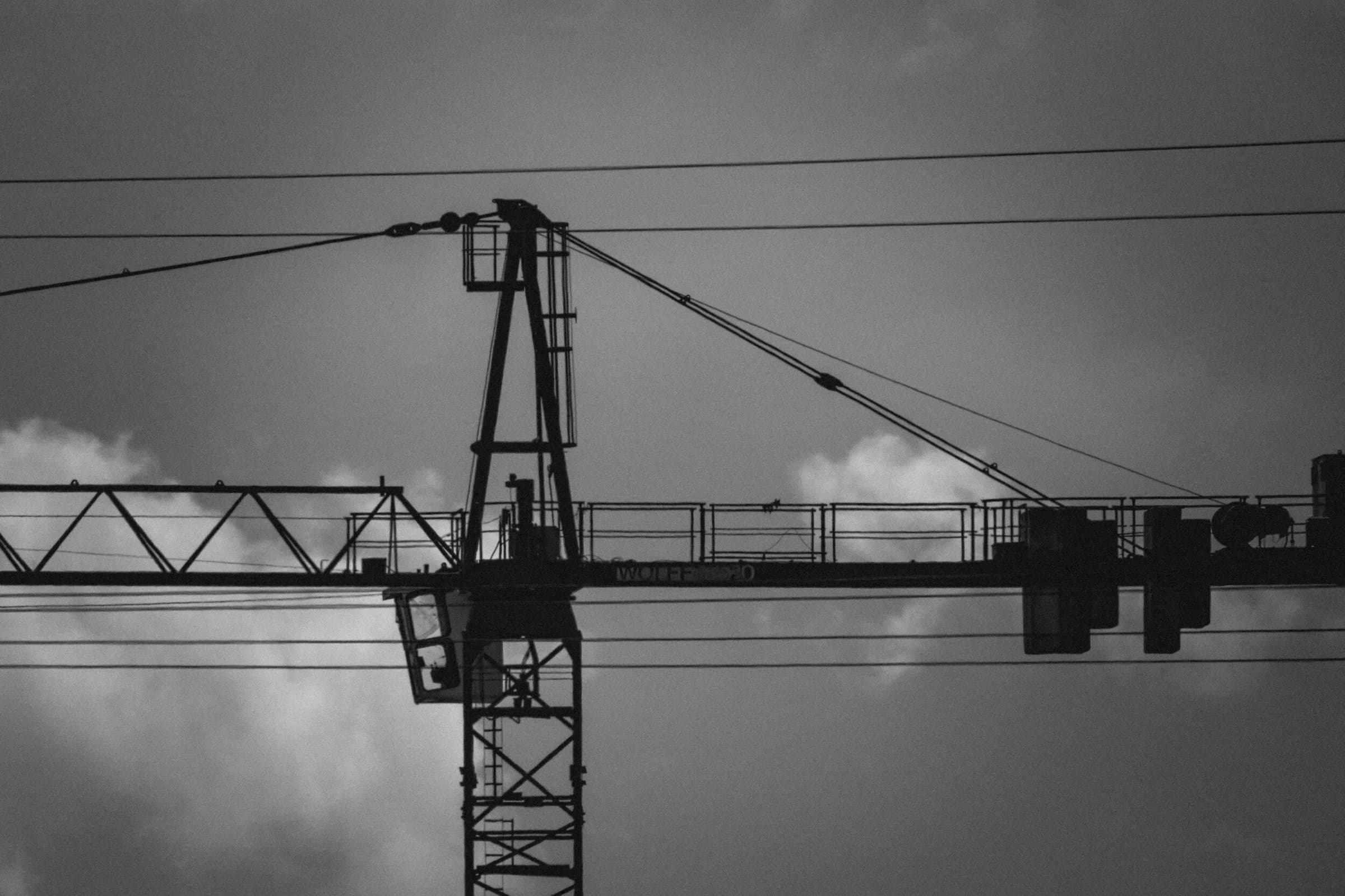 Black and white close-up of a tower crane jib and trolley against the sky