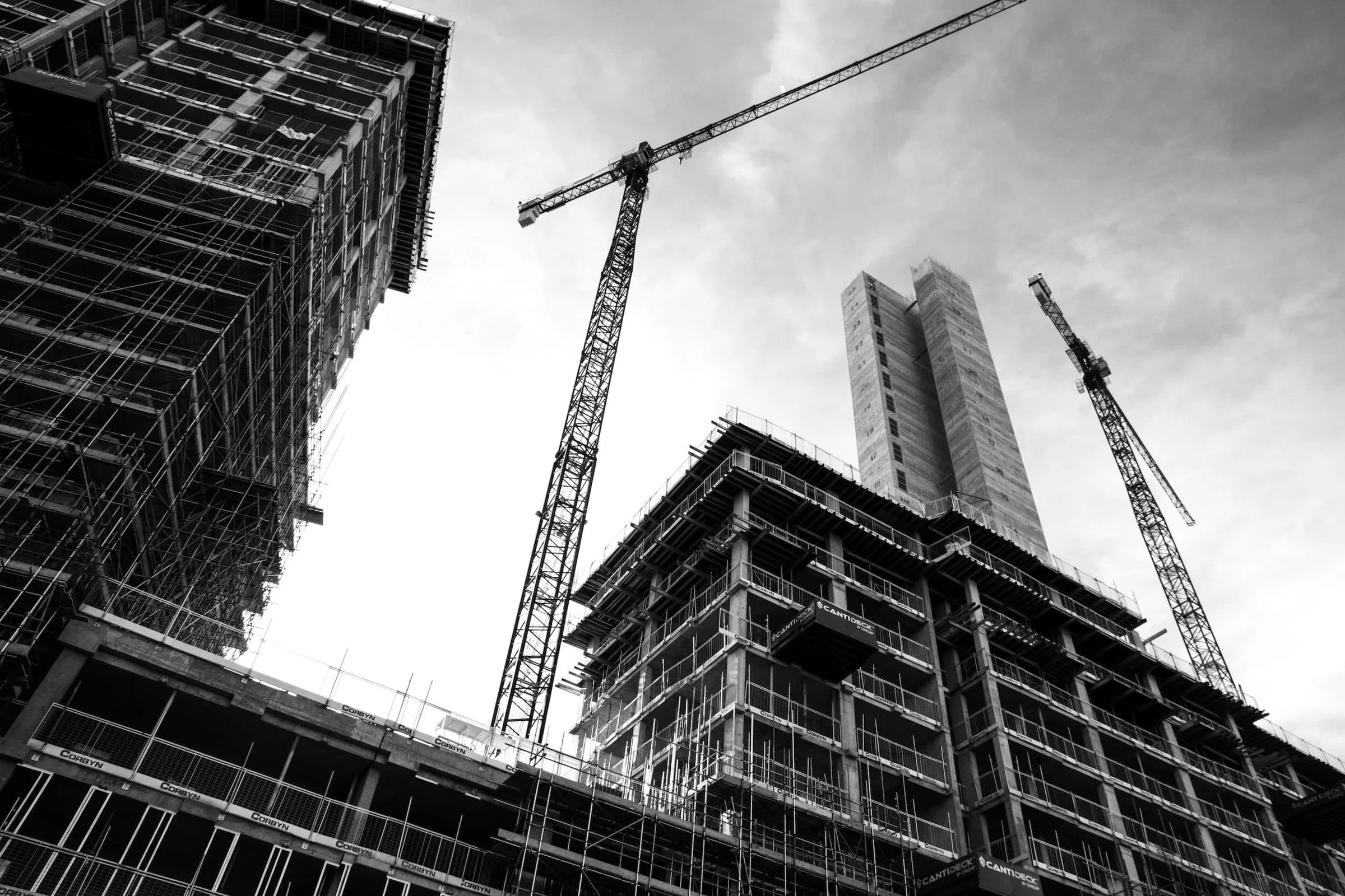Black and white photo of two tower cranes over a concrete high-rise under construction